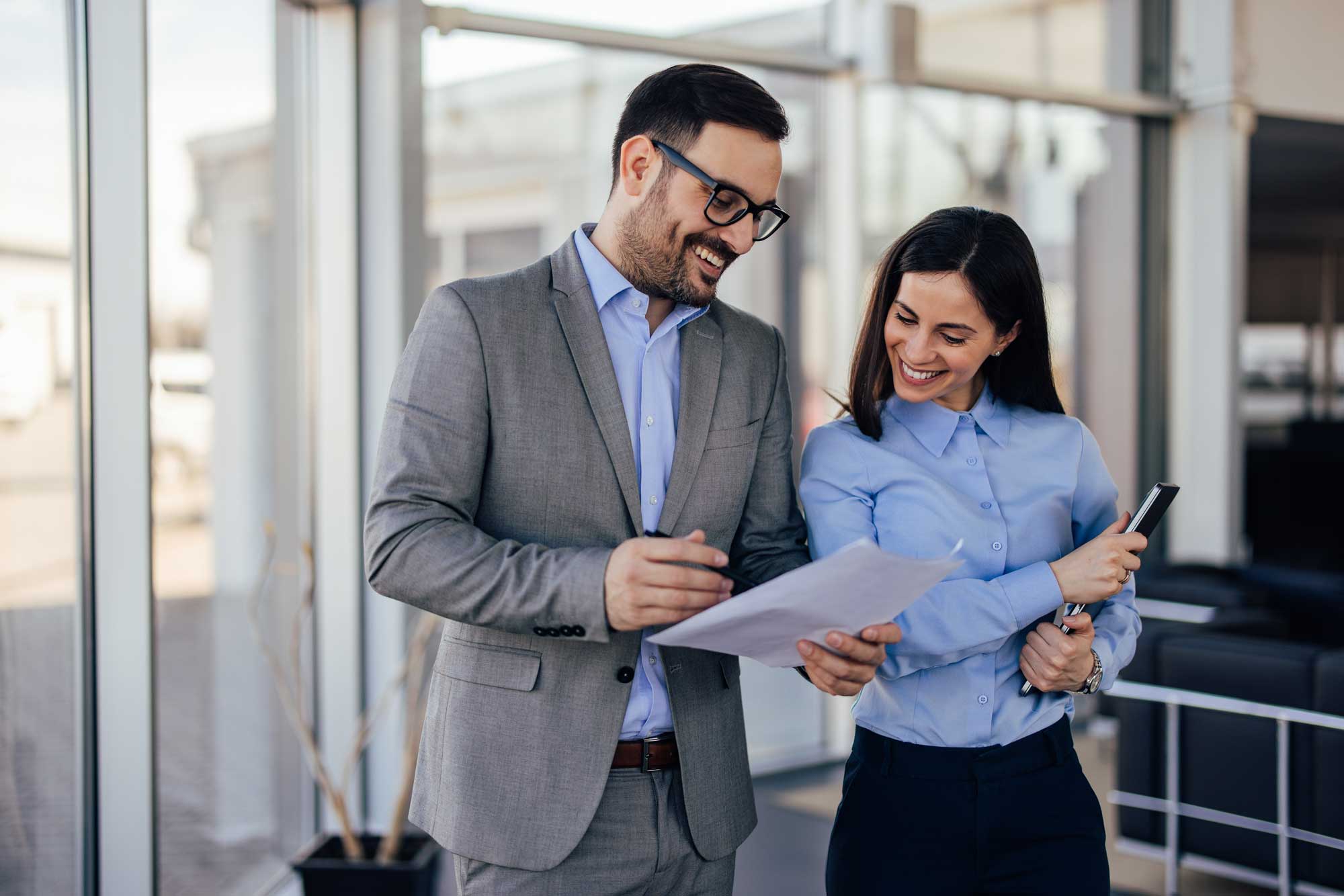 brunette_woman_and_a_man_with_glasses_on_reading_one_document_together_smiling